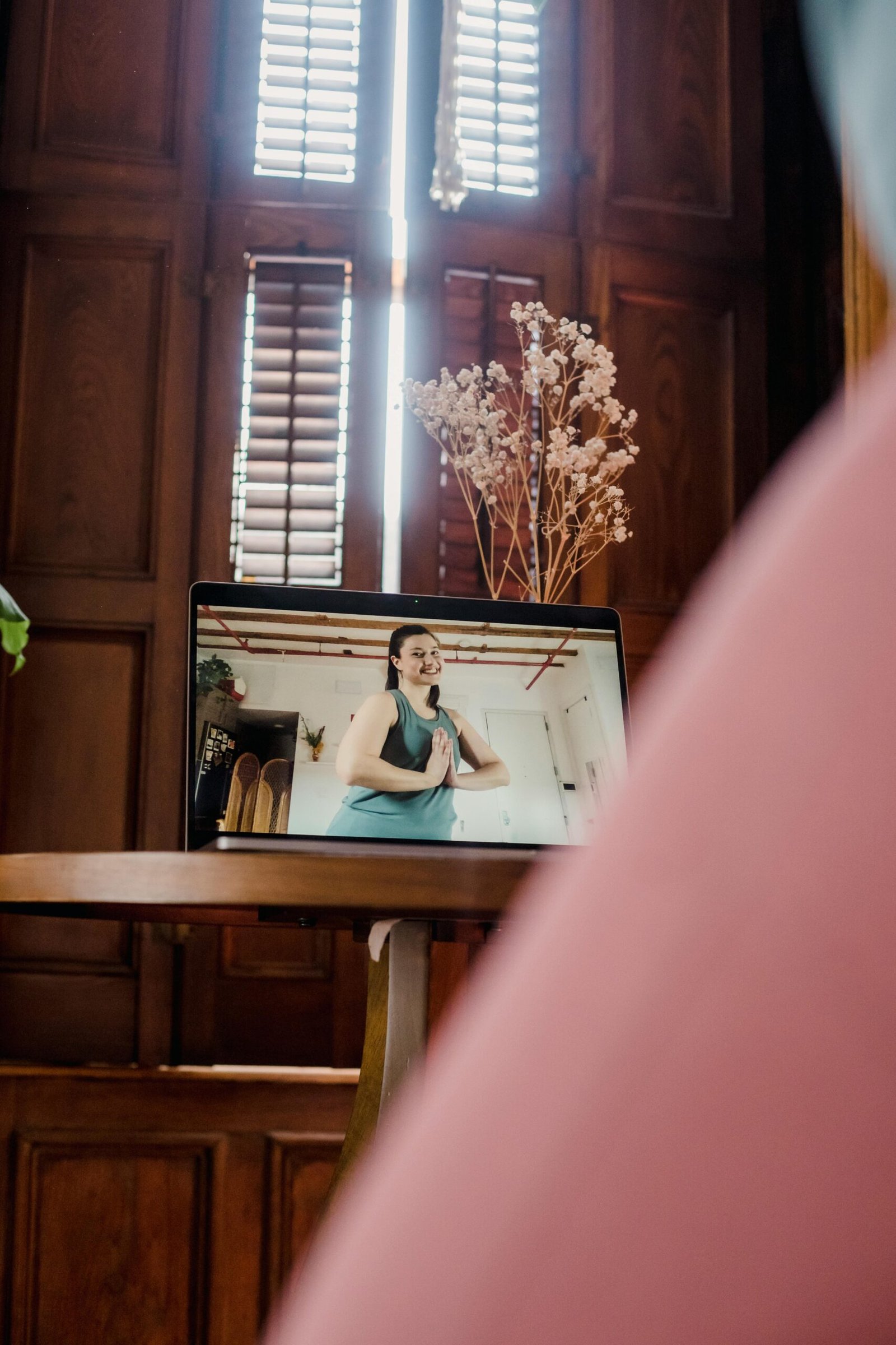 A woman teaching a yoga class via video on a laptop indoors, with natural light.